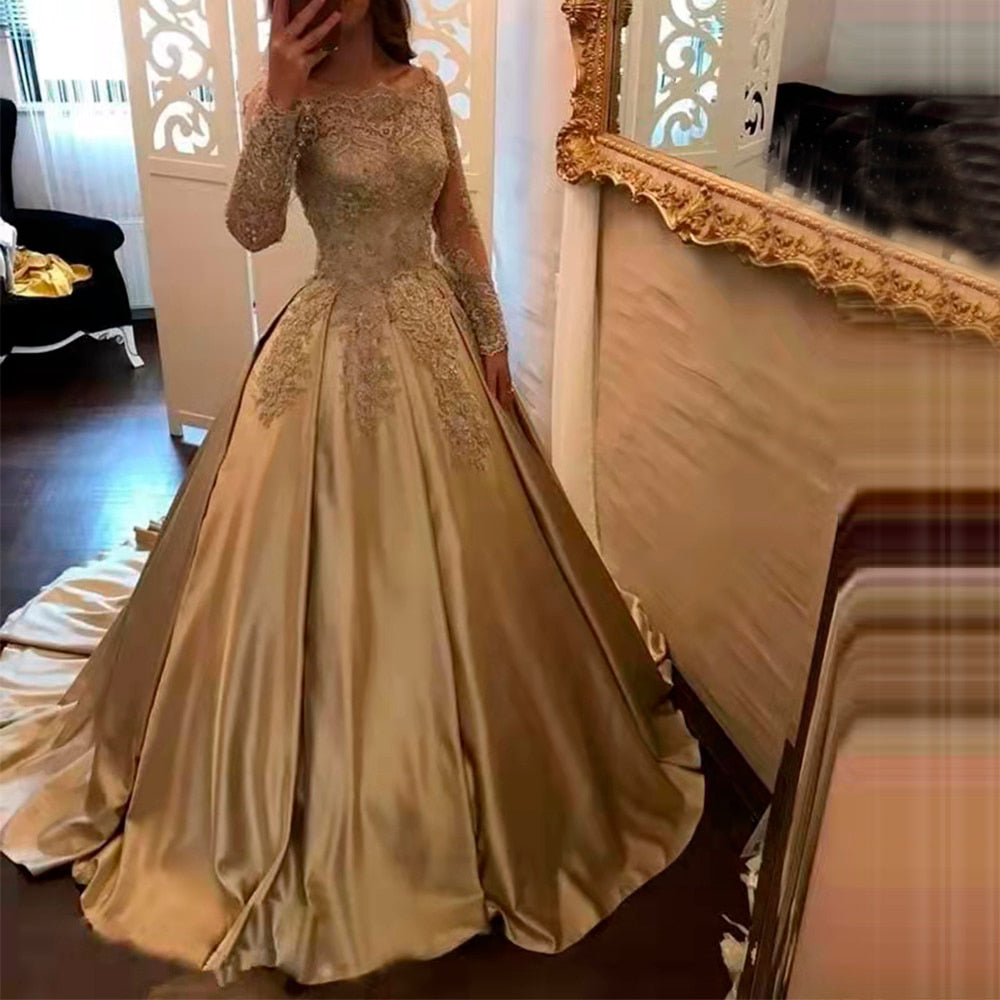 Woman in a luxurious, long-sleeved, gold ball gown with intricate lace details, poses in front of a large ornate mirror, creating an elegant atmosphere.