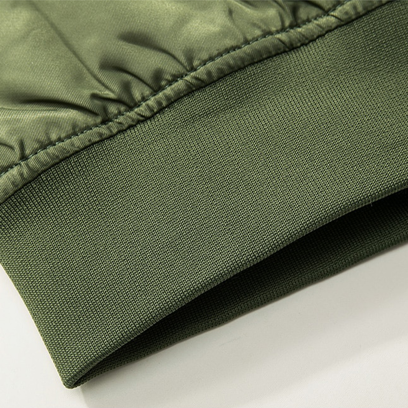Close-up of an olive green jacket cuff, showing fine stitching and a ribbed texture. The fabric has a slightly glossy appearance, indicating quality material.