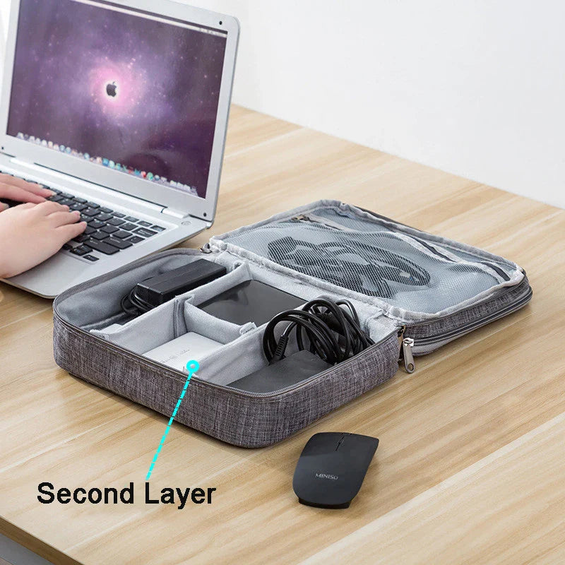 A laptop sits on a wooden desk beside an open organizer case with electronics, including cables and a phone.