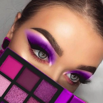 Close-up of a woman with bold, vibrant purple and pink eye makeup, partially hiding behind a matching eyeshadow palette, highlighting dramatic eye look.
