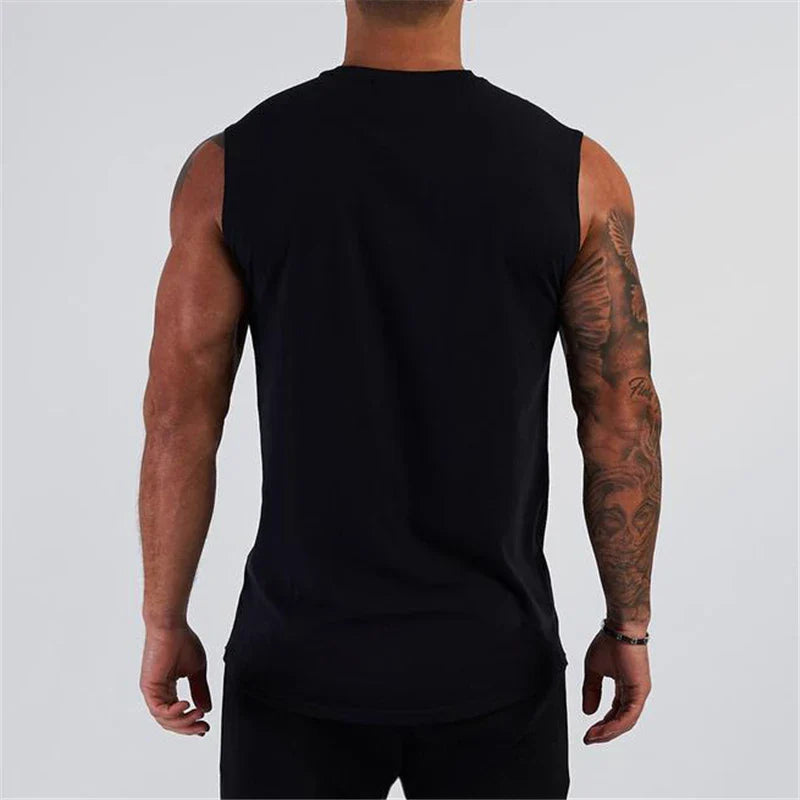 A muscular man with tattoos wears a sleeveless black shirt, viewed from the back against a neutral gray background.