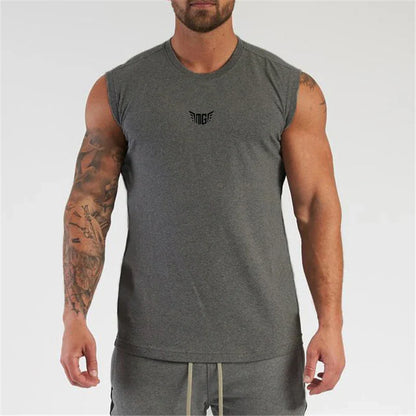 A muscular man with tattoos wears a sleeveless gray shirt, showcasing a logo on the chest and a confident pose.