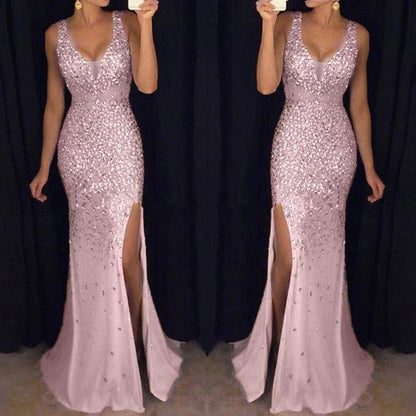A woman in a shimmering, sleeveless pink gown with a deep v-neck and high slit stands in front of a dark background, conveying elegance and glamour.
