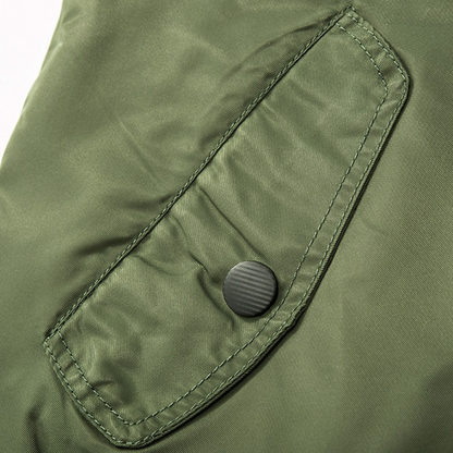 Close-up of a green fabric jacket with a stitched flap pocket secured by a black button. The fabric appears smooth and slightly reflective.