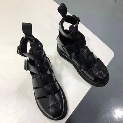 pair of black strappy sandals displayed on a white table, featuring a modern design and ankle strap for a secure fit.