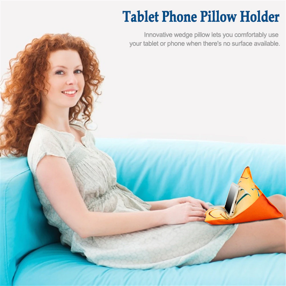 A woman sits on a blue couch, using a wedge-shaped pillow to support her tablet phone comfortably in her lap.