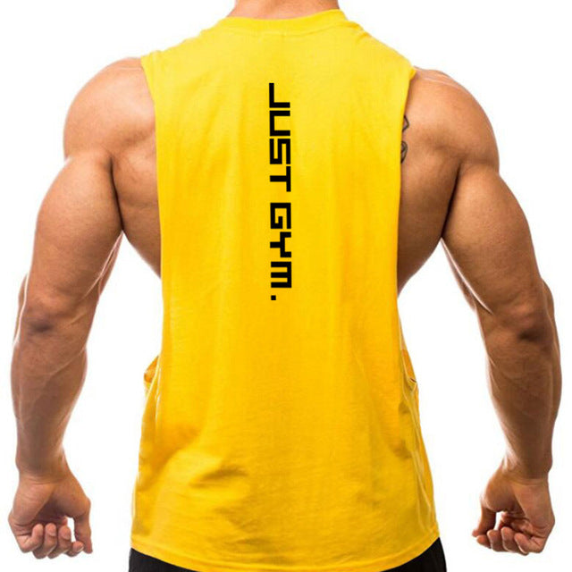 A man with muscular arms stands with his back to the camera, wearing a yellow sleeveless shirt featuring "JUST GYM." in bold black text.