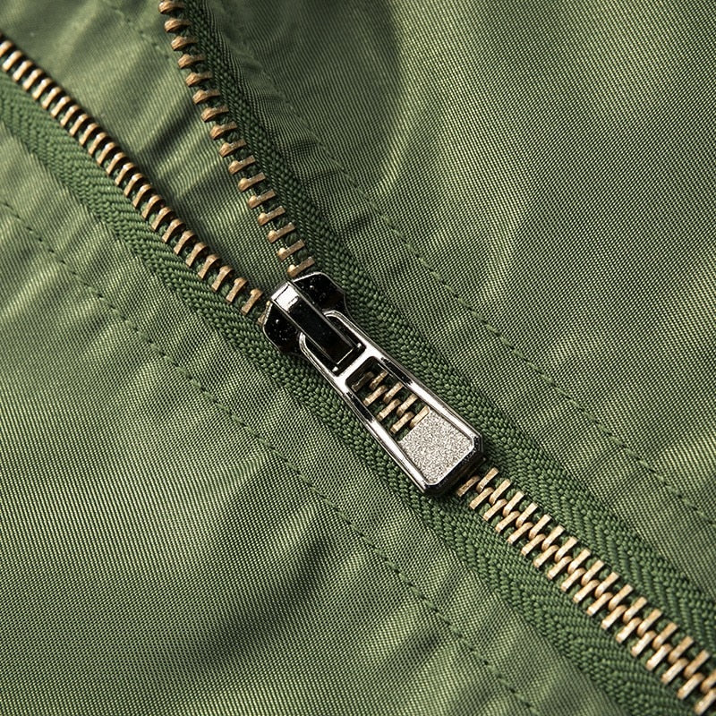 Close-up of a metal zipper on green fabric, showing detailed stitching and texture. The shiny silver zipper contrasts with the matte cloth surface.